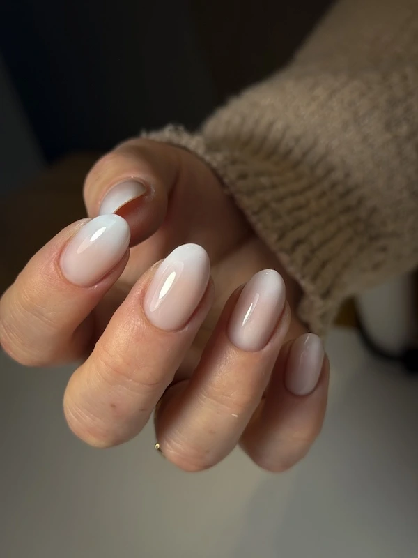 Apperçu des mains d'une cliente avec une pose sur ongles naturels mi-longs de couleur blanc avec baby boomer